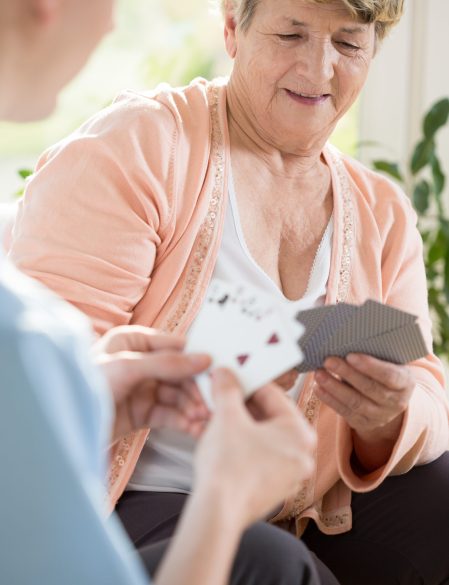 Older happy woman playing cards with her male nurse